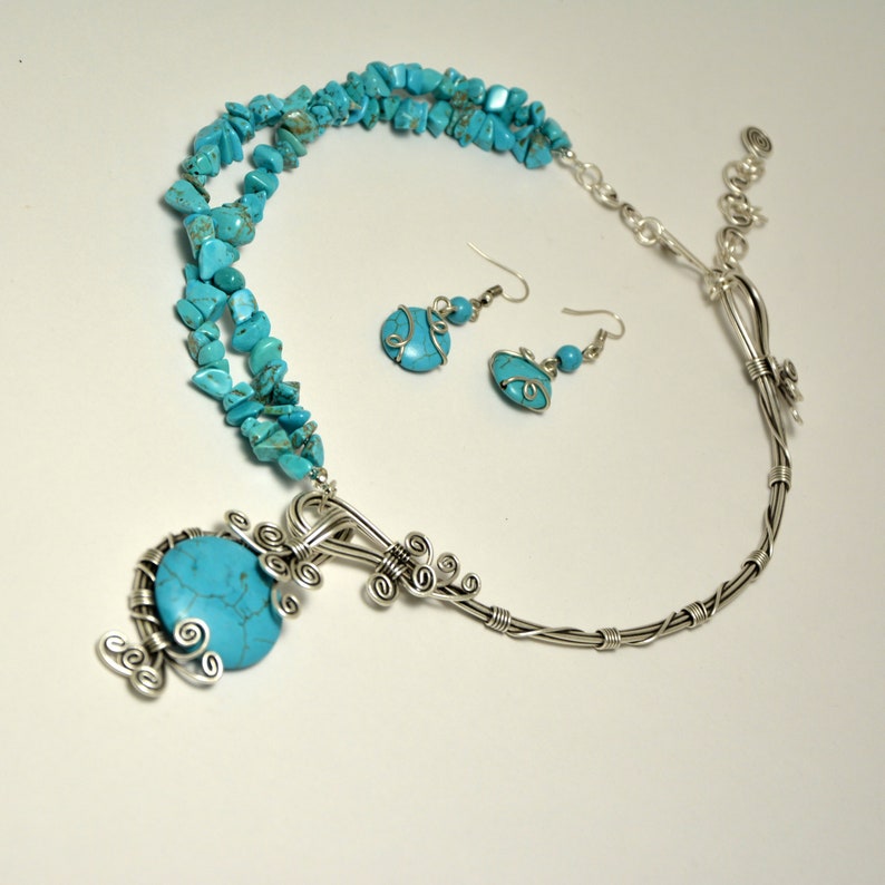 May include: A turquoise and silver necklace and earrings set. The necklace features a large turquoise stone pendant with silver wire detailing. The earrings are silver with turquoise stones.