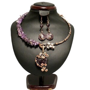 May include: A copper wire necklace and earrings set with amethyst stones. The necklace features a pendant with a large amethyst stone wrapped in copper wire. The earrings have smaller amethyst stones.