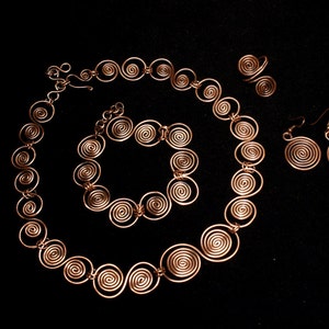 May include: A copper wire jewelry set with a necklace, bracelet, and earrings. The jewelry features a spiral design.