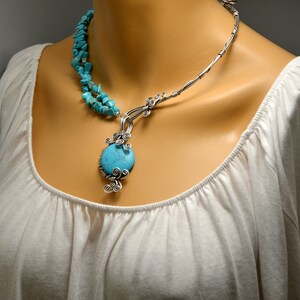May include: A silver wire necklace with a turquoise stone pendant. The necklace is made of multiple strands of wire and features a delicate, intricate design. The turquoise stone is round and has a smooth, polished surface.