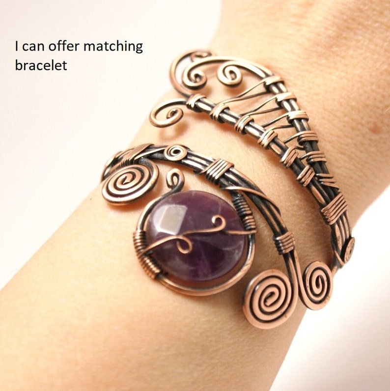 May include: A copper wire bracelet with a purple amethyst gemstone. The bracelet features a delicate, intricate design with swirls and loops.