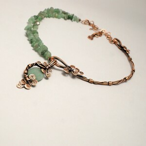 Peut inclure: Un collier en fil de cuivre avec un pendentif en pierre verte. Le pendentif est en forme de branche d'arbre avec des d&eacute;tails en fil de fer boucl&eacute;. Le collier est fait avec une double rang&eacute;e de pierres vertes.
