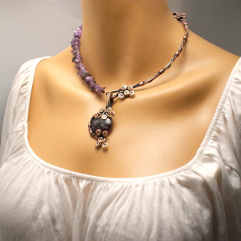 May include: A copper wire necklace with a large amethyst pendant. The pendant is surrounded by copper wire swirls. The necklace is made of small amethyst chips.