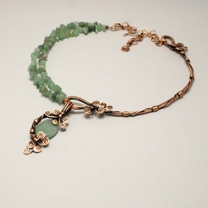 Peut inclure: Un collier en fil de cuivre avec un pendentif en pierre verte et des perles en pierre verte. Le pendentif est fait de fil de cuivre torsad&eacute; et fa&ccedil;onn&eacute; en un motif floral. Le collier est une pi&egrave;ce forte qui serait parfaite pour un look boh&egrave;me ou inspir&eacute; de la nature.