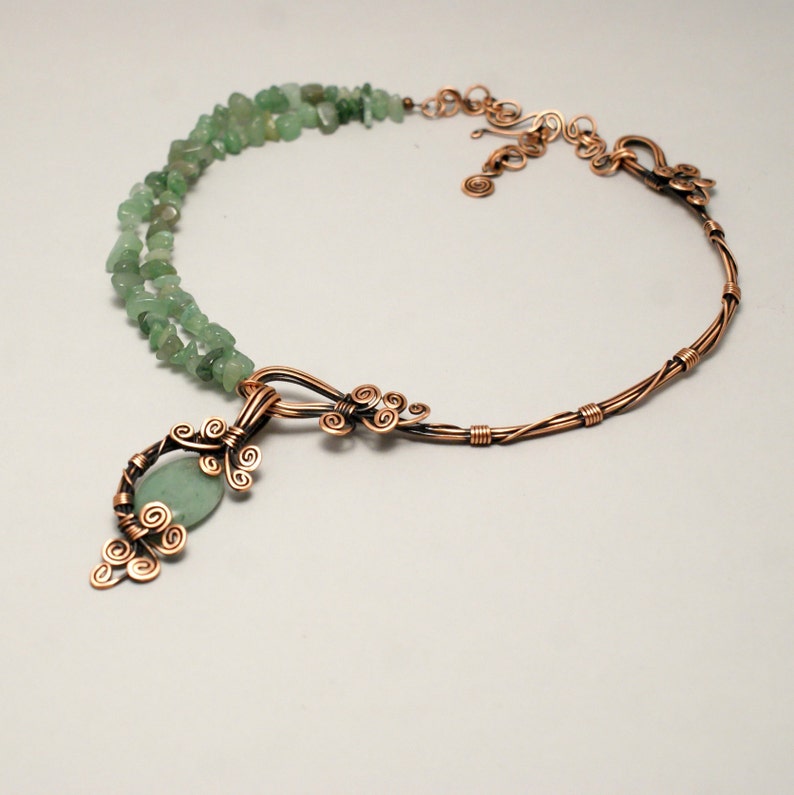 Peut inclure: Un collier en fil de cuivre avec un pendentif en pierre verte et des perles en pierre verte. Le pendentif est fait de fil de cuivre torsad&eacute; et fa&ccedil;onn&eacute; en un motif floral. Le collier est une pi&egrave;ce forte qui serait parfaite pour un look boh&egrave;me ou inspir&eacute; de la nature.