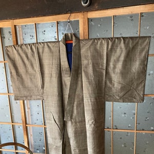 May include: A brown and beige patterned kimono hanging on a wooden hanger against a backdrop of a traditional Japanese sliding door.