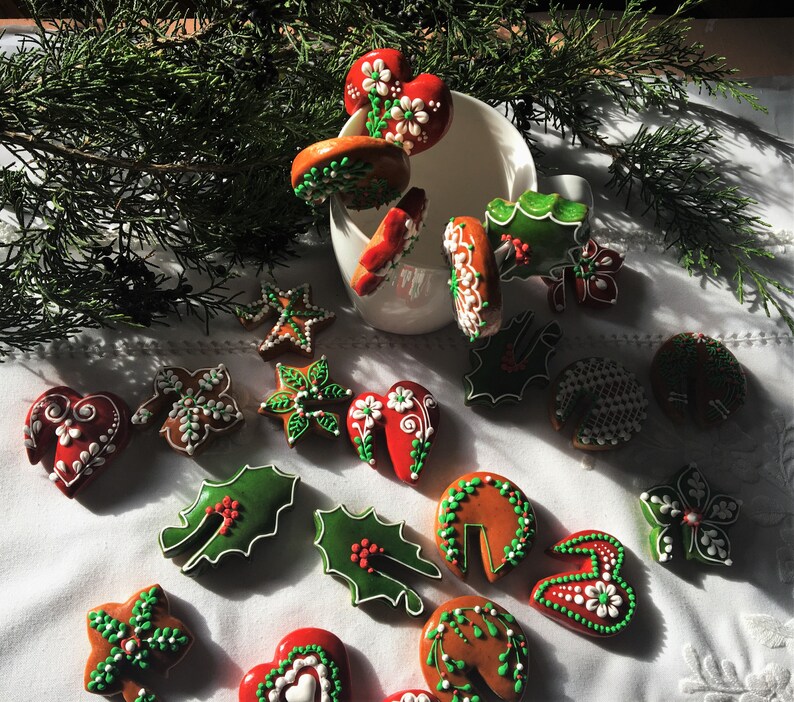 May include: An assortment of Christmas cookies decorated with green and white icing. The cookies are shaped like hearts, stars, leaves, and flowers. Some of the cookies are arranged in a white mug.