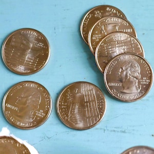 May include: A collection of United States quarter dollar coins, some loose and some rolled in paper. The coins are a golden color and feature the profile of George Washington and various designs on the reverse side.