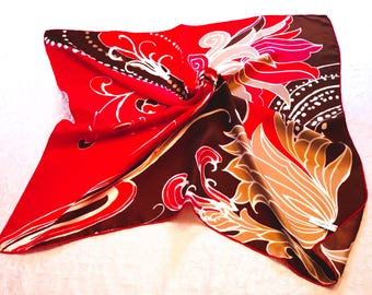 Könnte beinhalten: Ein quadratisches Tuch in einer kräftigen Farbpalette aus leuchtendem Rot und tiefem Schokoladenbraun. Der Stoff zeigt große, stilisierte Blumenmotive in Creme und Weiß, die durch komplizierte geschwungene Linien und Punktmuster ergänzt werden.