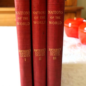 Può includere: Tre libri con copertina rigida rossa intitolati Nations of the World Hawthorne's United States, etichettati con numeri romani I, II e III in lettere dorate sui dorsi. I libri sono posizionati verticalmente, mostrando le copertine in tessuto rosso testurizzato.