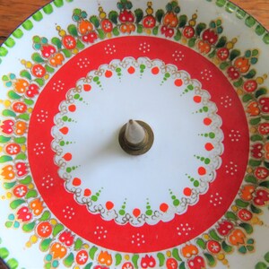 Op de afbeelding: Een decoratief serveerblad in vintage-stijl met een witte kern en een levendige rode rand. De lade heeft een bloemenontwerp in oranje, groen en geel, met een messing spil in het midden. De rand is groen met een blauwe rand.