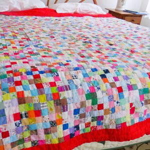 May include: A handmade quilt with a patchwork design, featuring a vibrant mix of colorful squares. The quilt has a bright red border and is spread across a bed. The quilt is a cozy bedding item.
