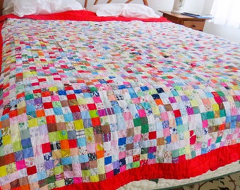 Könnte beinhalten: Handgefertigte Patchwork-Decke mit einer lebendigen Mischung aus bunten Quadraten. Die Decke hat einen leuchtend roten Rand und liegt auf einem Bett. Ein gemütliches Bettwäsche-Element.