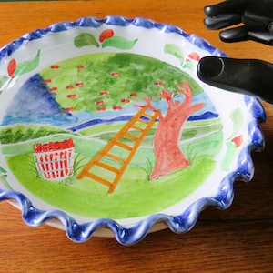 以下が含まれることがあります： 手描きのセラミックパイ皿。気まぐれな桜の果樹園のシーンが描かれています。 プレートは、青いボーダーのフリルエッジが特徴です。 内部には、木、はしご、さくらんぼのバスケットが描かれています。