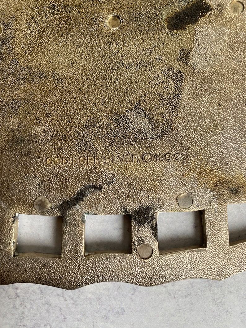 May include: Close-up of a gold-colored metal plate with a scalloped edge. The plate has a textured surface and several square cutouts. The text "SPRINGFIELD SILVER 1992" is engraved on the plate.