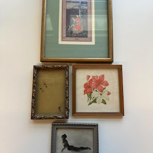 May include: A collection of four framed artworks: a vertical painting of a figure in red, an empty ornate rectangular frame, a square print of red and white flowers, and a small horizontal black and white photograph of a reclining figure.