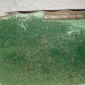 May include: Close-up of the bottom of a silver-plated object with a green felt backing. The text "Godinger Silver &copy; 1933" is printed on the bottom.