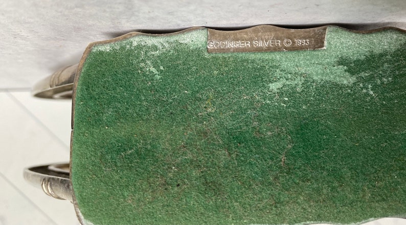 May include: Close-up of the bottom of a silver-plated object with a green felt backing. The text "Godinger Silver &copy; 1933" is printed on the bottom.