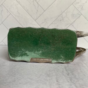 May include: Silver-toned metal bottle holder with a green felt base. The base has the text "SCHWEITZER BROS. 1973" printed on it.
