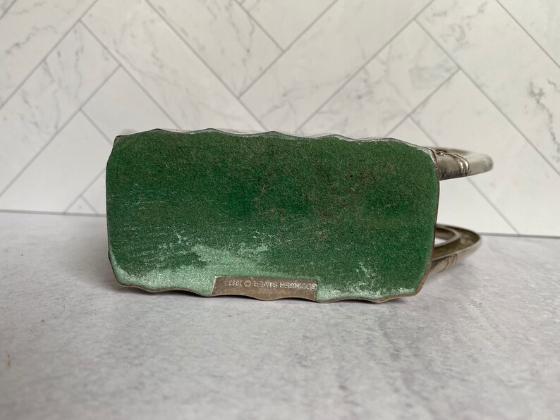 May include: Silver-toned metal bottle holder with a green felt base. The base has the text "SCHWEITZER BROS. 1973" printed on it.