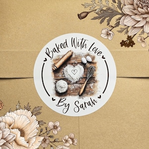 May include: White round sticker with a brown woodgrain background. The sticker has a brown rolling pin, a bowl of flour, two eggs, a whisk, and a heart drawn in flour. The text on the sticker reads "Baked With Love" and "By Sarah".