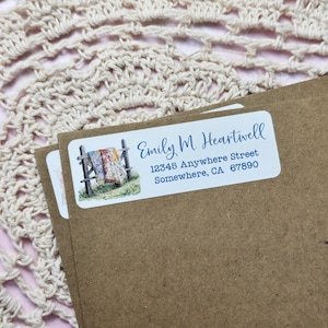 May include: A white return address label with a blue border and a watercolor illustration of a quilt hanging on a fence. The text on the label reads "Emily M. Heartwell, 12345 Anywhere Street, Somewhere, CA 67890".