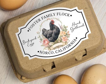 May include: A brown cardboard egg carton with a decorative label featuring a black hen illustration surrounded by flowers. The label reads "Foster Family Flock," "Backyard Eggs," "Hand Gathered," and "Norco, California."