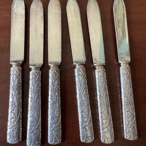 May include: Set of six silver butter knives with ornate floral designs on the handles.