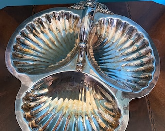 May include: A silver serving dish with three sections shaped like seashells. The dish has a handle in the center.