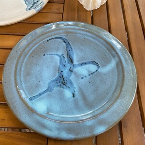 May include: A light blue ceramic plate with a white and gray glaze. The plate has a raised rim and a subtle swirl design.