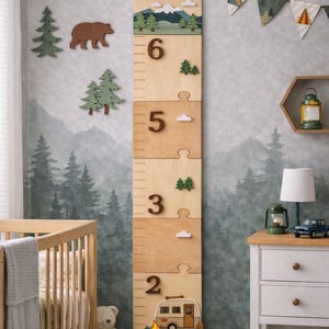 May include: A wooden growth chart with the name "Salvador" at the top, featuring a camping theme. The chart has measurements in feet and inches, with decorative elements like trees, clouds, and a camper van. The background is a forest mural.