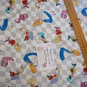 May include: White fabric with a chequered pattern featuring Alice in Wonderland characters, including Alice, the Mad Hatter, the Cheshire Cat, and the White Rabbit. The fabric is printed with colourful illustrations of the characters.