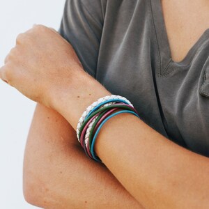 Könnte beinhalten: Eine Person trägt ein graues T-Shirt mit einem Stapel bunter Armbänder am Handgelenk.