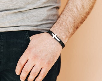 Puede incluir: Un brazalete de cuero negro con un dije de cruz de plata.