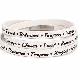 May include: A white wrap bracelet featuring dark brown text printed along the band. The words include Loved, Redeemed, Forgiven, Adopted, Known, Chosen, and Beloved, separated by small dots. The bracelet has a metallic silver magnetic clasp.