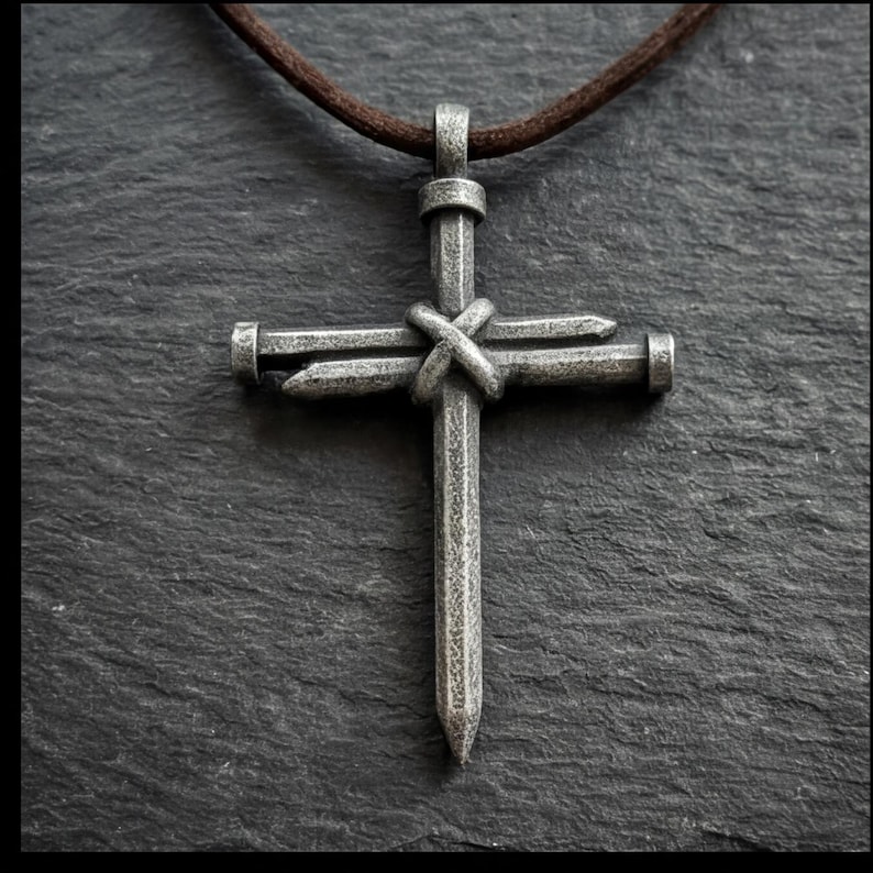 May include: A silver-colored cross pendant crafted from nails, knotted at the center, with a brown leather cord. The cross has a rustic, handmade appearance, set against a textured, stone-like background.