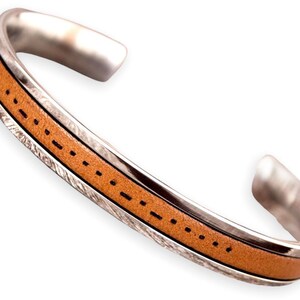 K&ouml;nnte beinhalten: Ein silbernes Armreif-Armband mit einem hellbraunen Lederband. Das Lederband ist mit schwarzem Faden gen&auml;ht. Das Armband hat eine strukturierte Silberoberfl&auml;che an den Seiten.