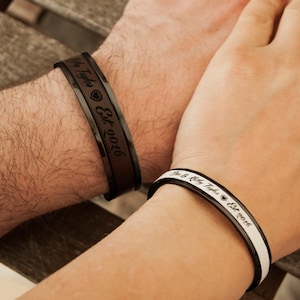 May include: A pair of black and white bracelets with engraved text. The bracelet on the left says "My Taylor Est. 2016" and the bracelet on the right says "We are a pretty big deal Est. 2016".