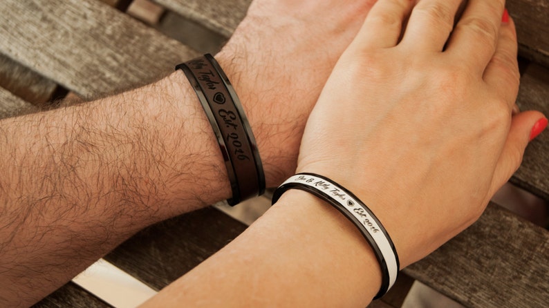 May include: A pair of black and white bracelets with engraved text. The bracelet on the left says "My Taylor Est. 2016" and the bracelet on the right says "We are a pretty big deal Est. 2016".