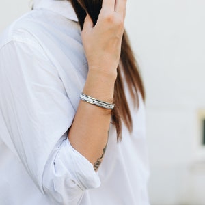 May include: A silver bracelet with a white band and the coordinates "47.2486&deg; N 12.0964&deg; E" engraved on it.