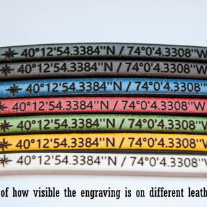 May include: A close-up of seven leather straps in different colors, each with the same engraved text: "40&deg;12'54.3384"N / 74&deg;0'4.3308"W". The colors are black, dark brown, blue, red, green, yellow, and white. The text is visible on each strap, but the visibility varies depending on the color of the leather.