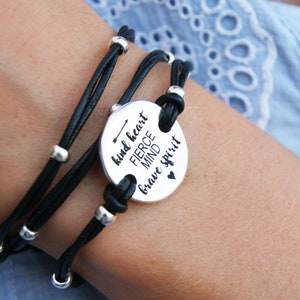 May include: A black leather wrap bracelet with silver beads and a round silver charm that reads "kind heart fierce mind brave spirit" with an arrow and a heart.
