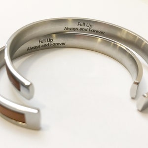 May include: Two silver bracelets with a brown leather inlay. The bracelets are engraved with the words "Full Up Always and Forever".