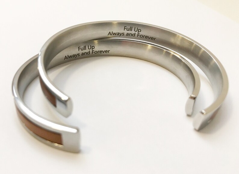 May include: Two silver bracelets with a brown leather inlay. The bracelets are engraved with the words "Full Up Always and Forever".