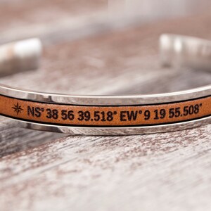May include: A silver and brown leather cuff bracelet with the coordinates "NS 38 56 39.518" EW 9 19 55.508" engraved on it.