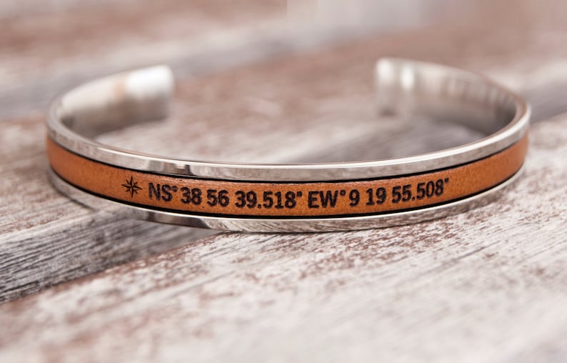 May include: A silver and brown leather cuff bracelet with the coordinates "NS 38 56 39.518" EW 9 19 55.508" engraved on it.