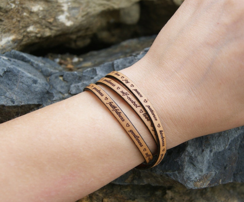 Puede incluir: Un brazalete de cuero de triple vuelta con las palabras "love", "joy", "peace", "patience", "kindness", "goodness", "faithfulness", "gentleness", "self-control" grabadas en &eacute;l.