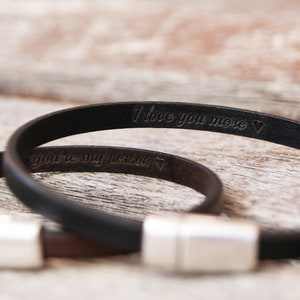 May include: Two leather bracelets with silver clasps. The black bracelet has the inscription "I love you more" and the brown bracelet has the inscription "you're my person".