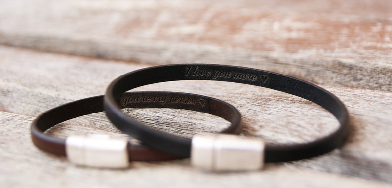 May include: Two leather bracelets with silver clasps. The black bracelet has the inscription "I love you more" and the brown bracelet has the inscription "you're my person".