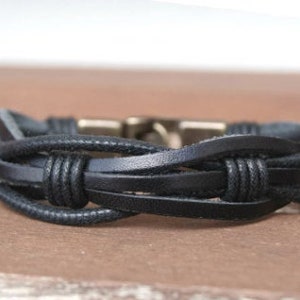 May include: A black leather bracelet with a braided design and a metal clasp.